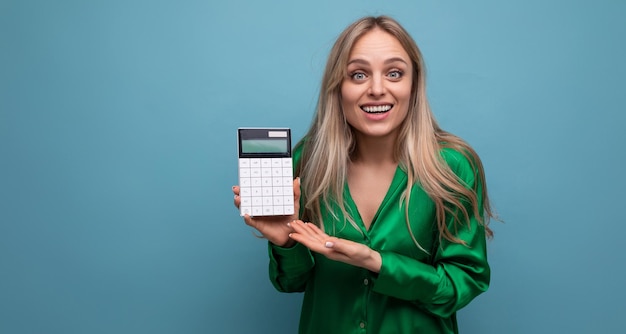 Foto chica rubia con estilo europea agradablemente perpleja con una calculadora sobre un fondo azul