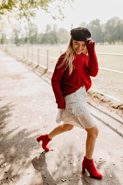 Chica rubia con estilo en suéter rojo teniendo fiesta con grandes emociones al aire libre Chica sonriente bailando con alegría y felicidad en el parque