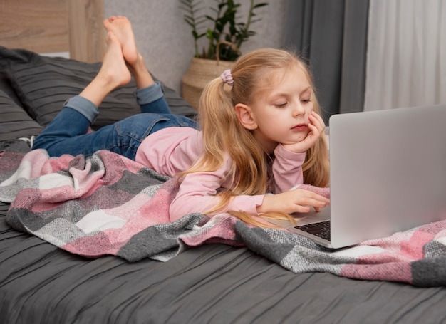 Chica rubia estudia en casa en línea con un portátil en la cama
