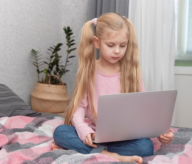 Chica rubia estudia en casa en línea con un portátil en la cama