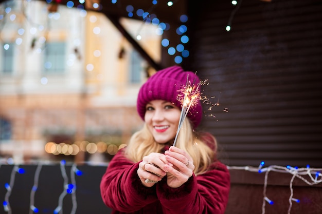 Chica rubia expresiva sosteniendo brillantes luces de Bengala en la feria de Navidad en Kiev. Efecto de desenfoque