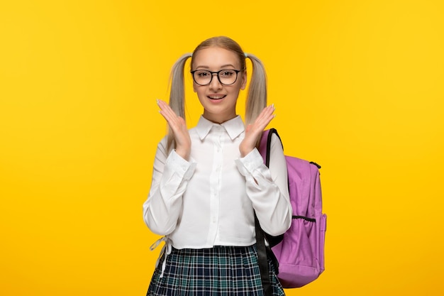 Chica rubia feliz del día mundial del libro con las manos saludando y mochila rosa