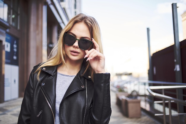 Chica rubia con gafas de sol y una chaqueta de cuero en la calle de la ciudad