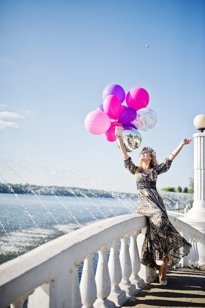 Foto chica rubia con globos en despedida de soltera contra el lago.