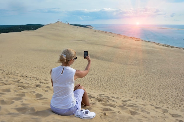 Chica rubia haciendo selfie para instagram en Pyla dune la duna de arena más grande de Europa