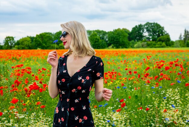 Chica rubia en un hermoso vestido en el campo de amapolas en verano