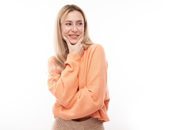 Una chica rubia inteligente con un mentón casual piensa que las dudas toman una decisión aislada en el fondo del estudio blanco