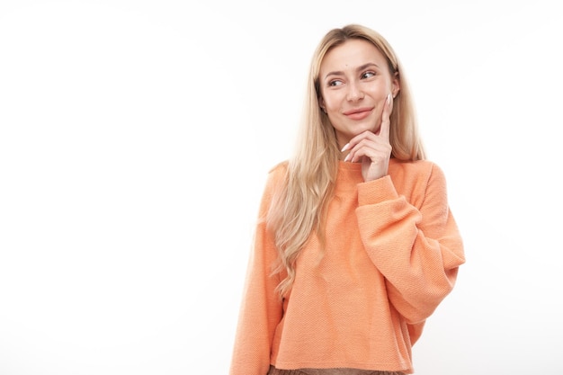 Una chica rubia inteligente con un mentón casual piensa que las dudas toman una decisión aislada en el fondo del estudio blanco