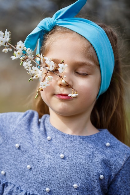 Chica rubia joven de pie en un jardín floreciente. Cereza floreciente. Retrato de niña hermosa. Cerca de la pequeña cara de modelo. Sakura floreciendo, tarde de primavera