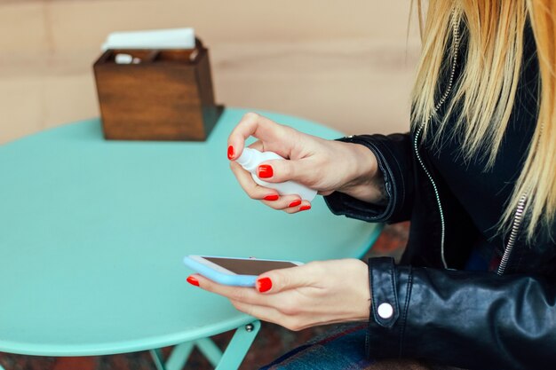 Foto una chica rubia con manicura roja trata el teléfono con un desinfectante de gérmenes.