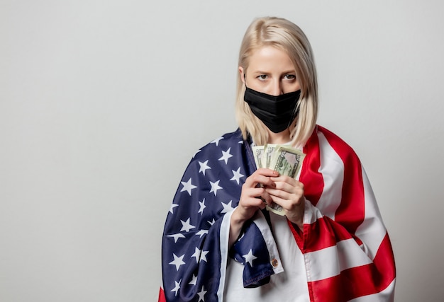 Chica rubia en mascarilla con bandera de Estados Unidos y dinero