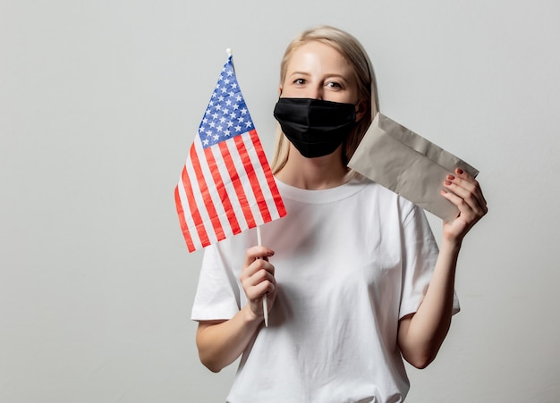 Chica rubia en mascarilla con bandera de Estados Unidos y dinero