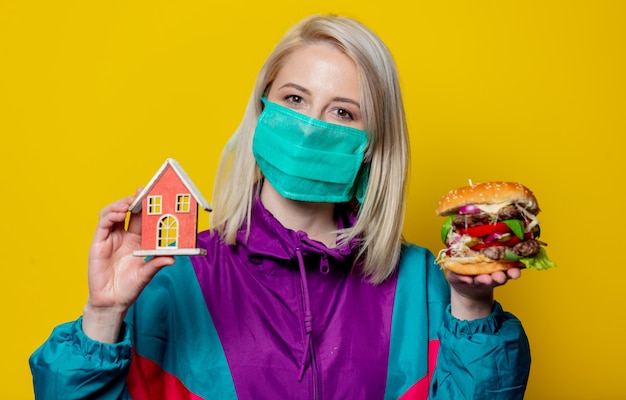 Chica rubia en mascarilla con hamburguesa y casita