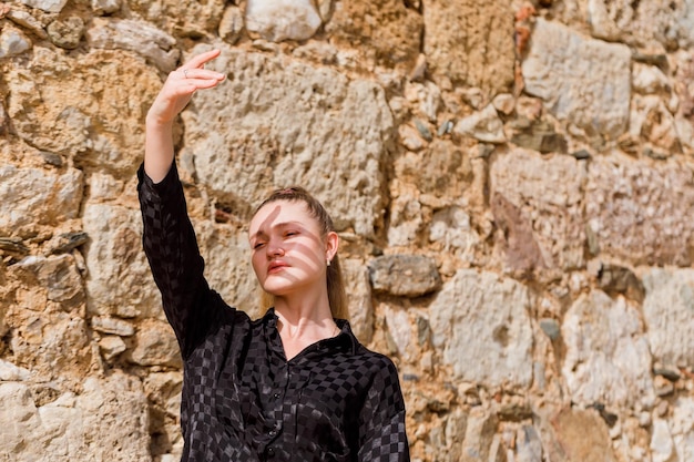 La chica rubia mira a la izquierda con vestido negro sobre fondo de piedra