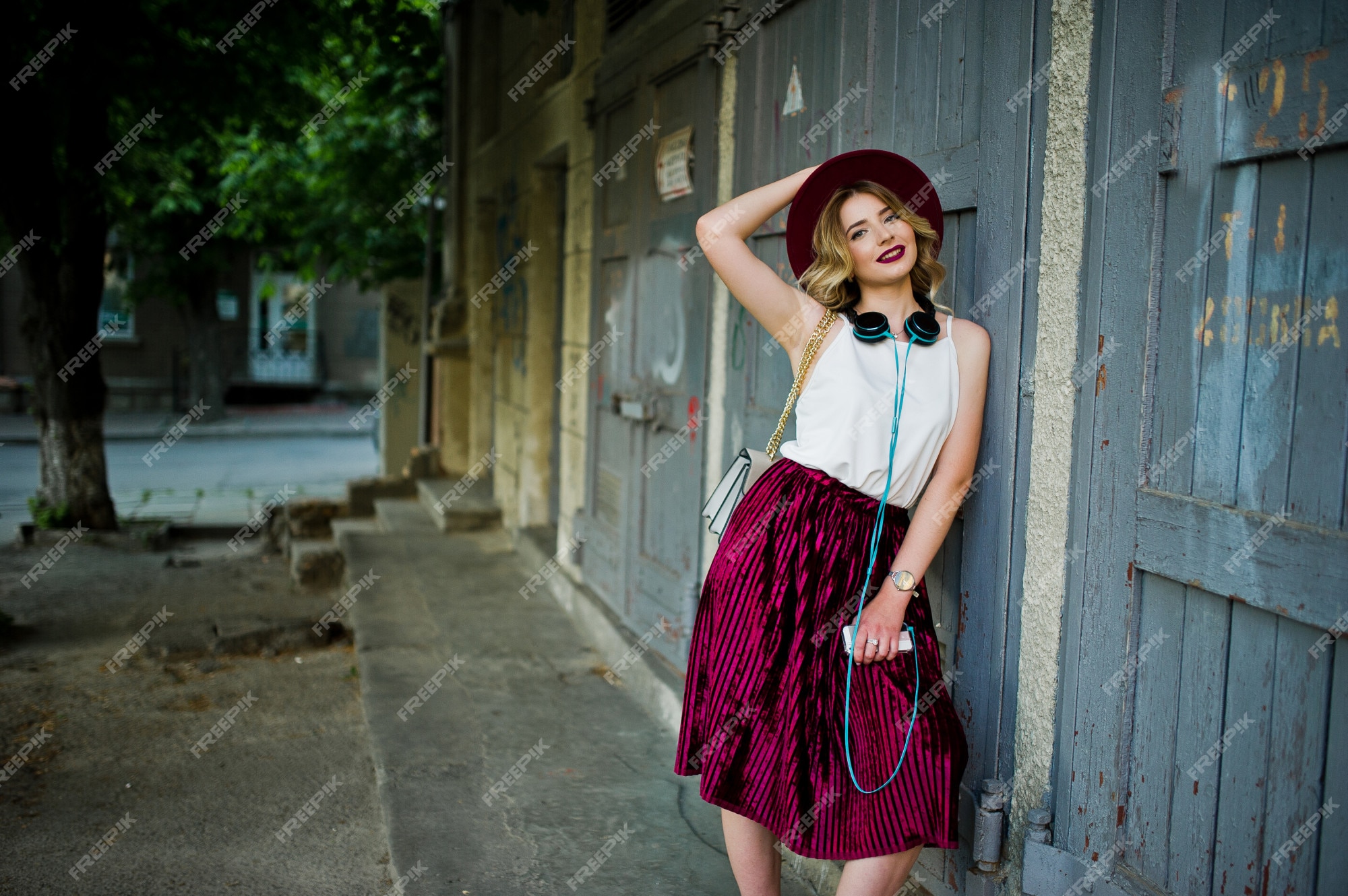 rubia moda y bella con elegante falda de terciopelo rojo de terciopelo, blusa blanca y sombrero, posada con teléfono y auriculares. | Foto Premium