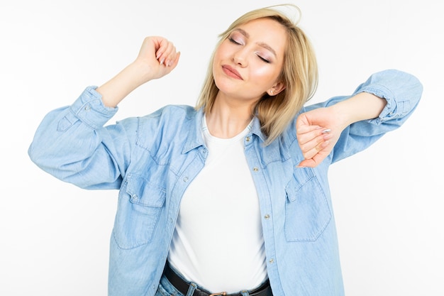 Chica rubia de moda con una camisa azul de mezclilla está bailando enérgicamente sobre un fondo blanco de estudio.