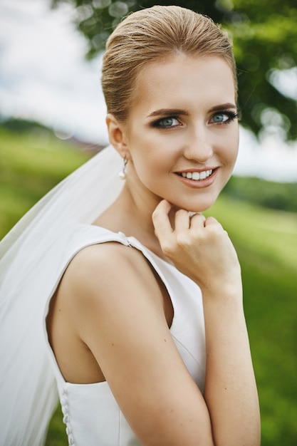 Chica rubia modelo con increíbles ojos azules y elegante peinado de novia sonriendo y posando al aire libre