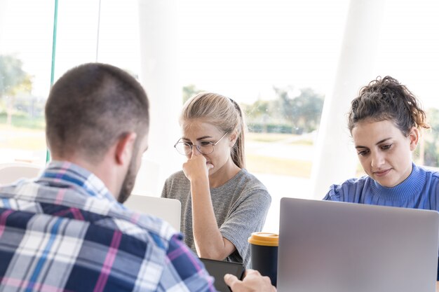 Chica rubia pensativa junto a un grupo de jóvenes que trabajan juntos en un coworking