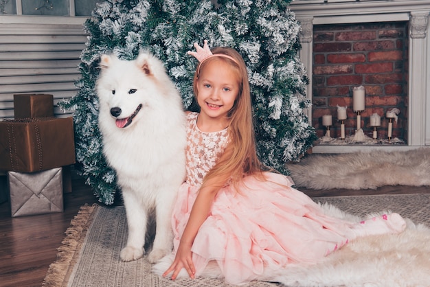 Chica rubia y perro Samoyedo por el árbol de año nuevo.