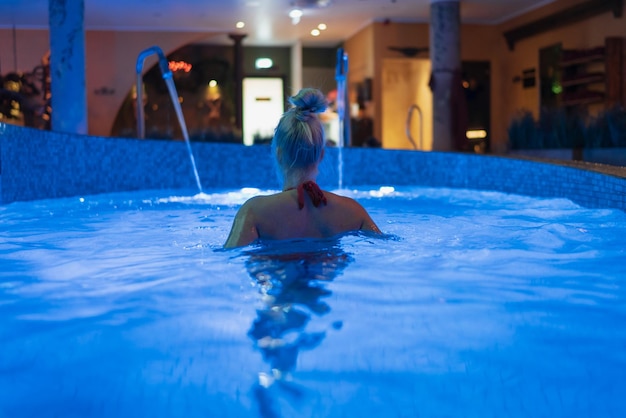 Chica rubia en una piscina de spa vista desde atrás Iluminación de paneles de hielo de color azul Foto de alta calidad