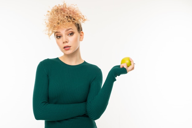 chica rubia rizada con una buena figura sostiene una manzana verde en su mano en blanco con copyspace