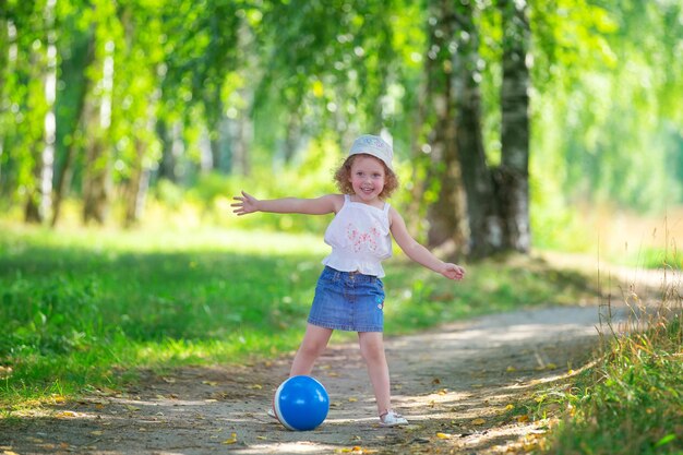 chica rubia rizada jugando con una pelota de goma en un parque de verano