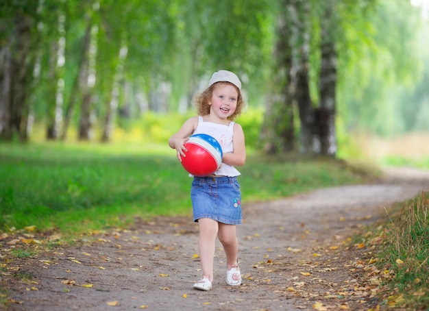 chica rubia rizada jugando con una pelota de goma en un parque de verano
