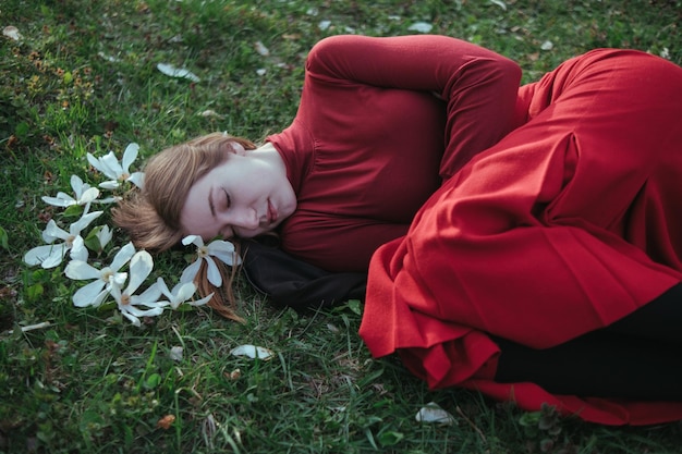 Una chica rubia de rojo yace en la primavera sobre la hierba rodeada de flores de magnolia