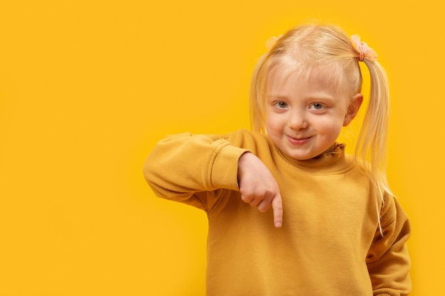 Chica rubia sonriente con dos colas apunta su dedo hacia abajo Retrato sobre fondo amarillo Copiar espacio