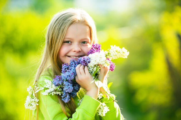 Chica rubia sonriente de pie en un jardín floreciente retrato lila floreciente de una hermosa niña