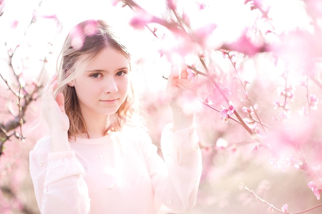 Chica rubia sonriente posando en flores de durazno rosa cerrar