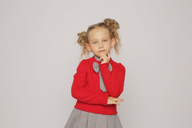 una chica rubia con un traje escolar, un vestido gris y un jersey rojo muestra emociones