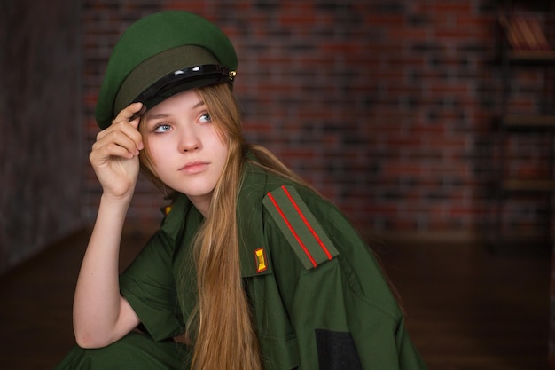 Chica rubia con uniforme militar y sombrero de invierno en el fondo de una pared de ladrillos