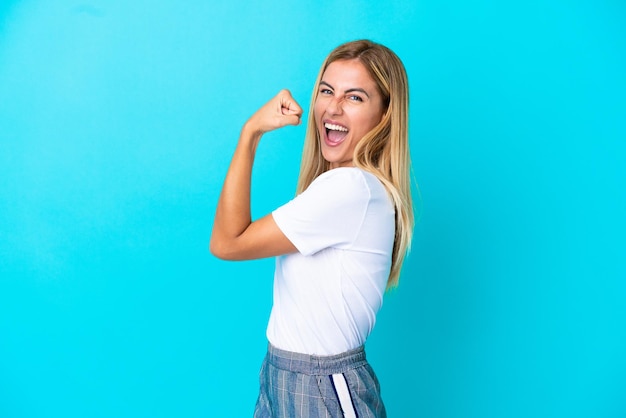 Chica rubia uruguaya aislada sobre fondo azul celebrando una victoria