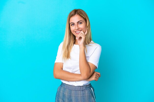 Chica rubia uruguaya aislada sobre fondo azul feliz y sonriente