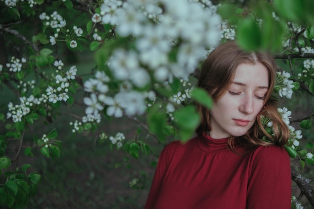 Una chica rubia vestida de rojo se une con la naturaleza en un jardín de árboles en flor