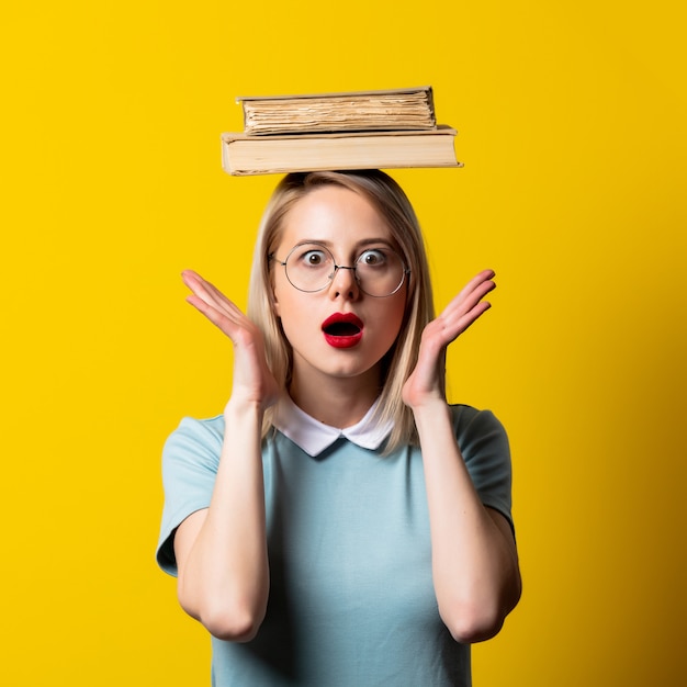 Chica rubia con vestido azul y gafas con libros sobre espacio amarillo