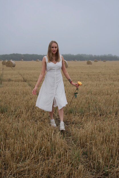 Chica rubia en un vestido blanco con lunares camina por el campo fardos de heno en el fondo