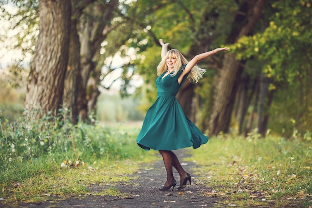 Una chica rubia con un vestido largo verde gira alrededor de un robledal