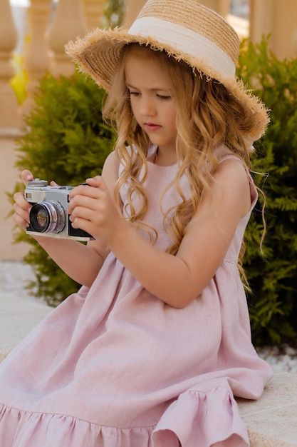 Una chica rubia con un vestido de lino rosa y un sombrero de paja sostiene una cámara en sus manos