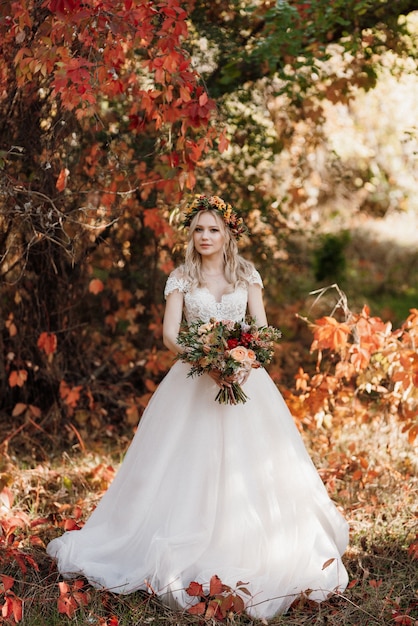 Chica rubia en un vestido de novia en el bosque de otoño con el telón de fondo de uvas rojas silvestres