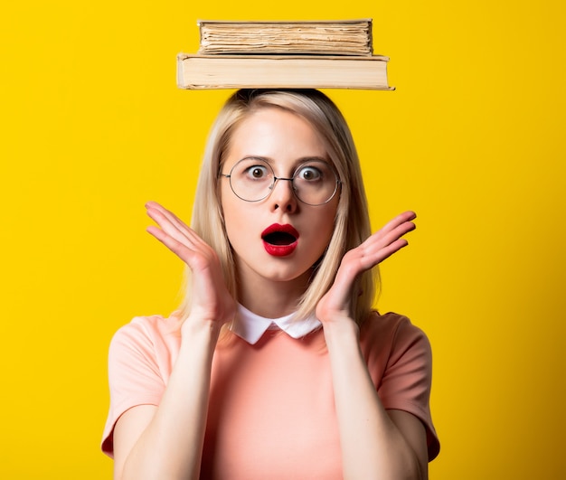 Chica rubia en vestido rosa y gafas con libros sobre espacio amarillo