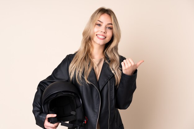 Chica rusa con un casco de moto en pared beige con pulgares arriba gesto y sonriendo