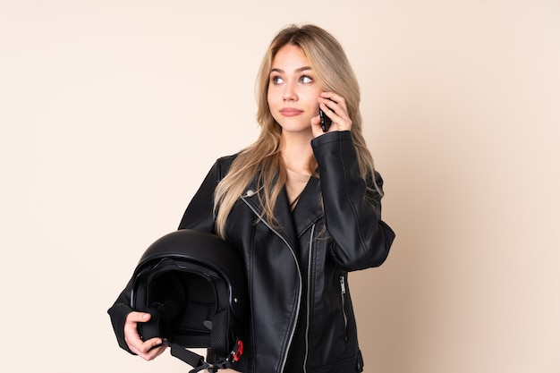 Chica rusa con un casco de moto en la pared de color beige con café para llevar y un móvil