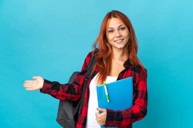 Chica rusa estudiante adolescente en azul extendiendo las manos hacia un lado para invitar a venir