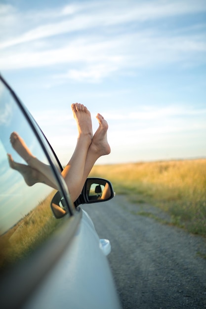 Chica sacando los pies descalzos por la ventana de un coche. Concepto de libertad y aventura.