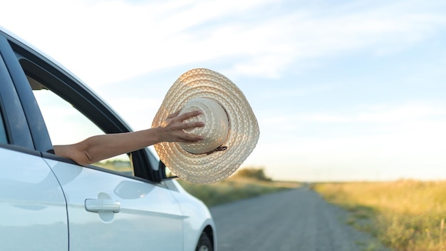 Chica sacando un sombrero con la mano por la ventana de un coche. Concepto de libertad y aventura.