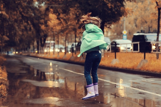 chica saltando en los charcos en la lluvia de otoño