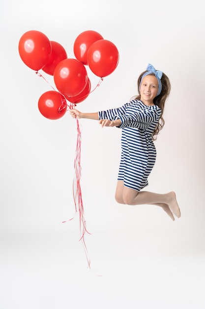 Chica en salto sosteniendo un gran montón de globos rojos en una mano y sonríe alegremente mirando a la cámara