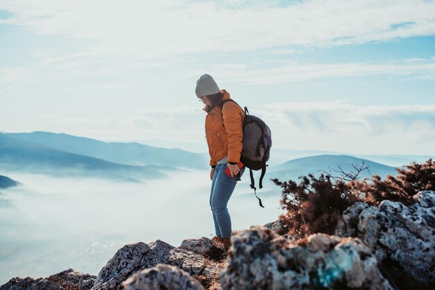 Una chica de senderismo con una mochila en la espalda mira la mañana desde la cima de la montaña.